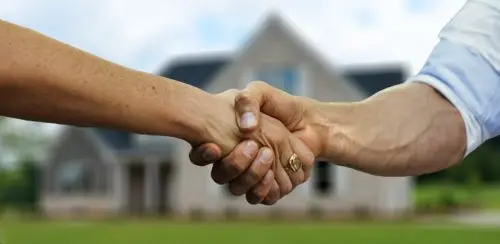 man and woman shaking hands in front of a house