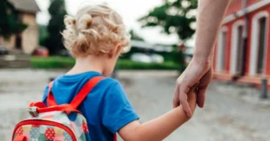 A parent holding the hand of a young child with a backpack