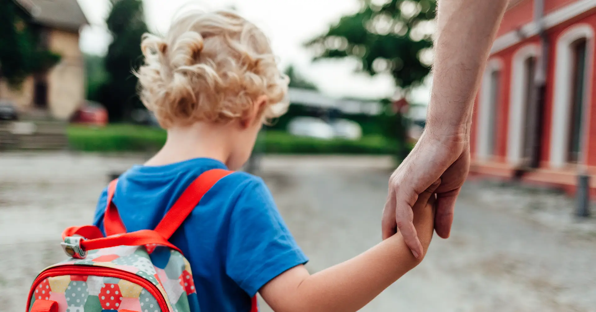 A parent holding the hand of a young child with a backpack